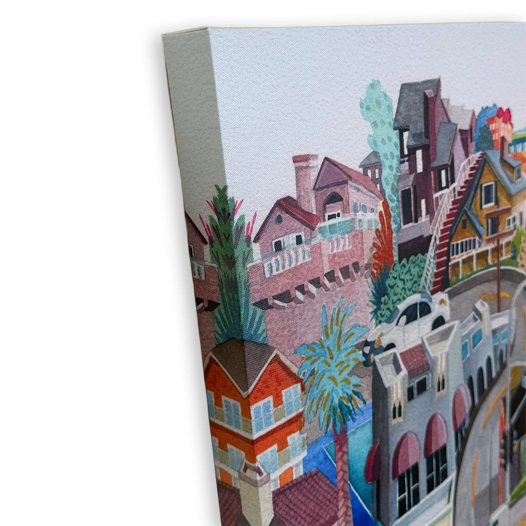 A watercolor-style canvas print showing a colorful coastal town or harbor scene with buildings, palm trees, and boats, photographed at an angle against a white background.