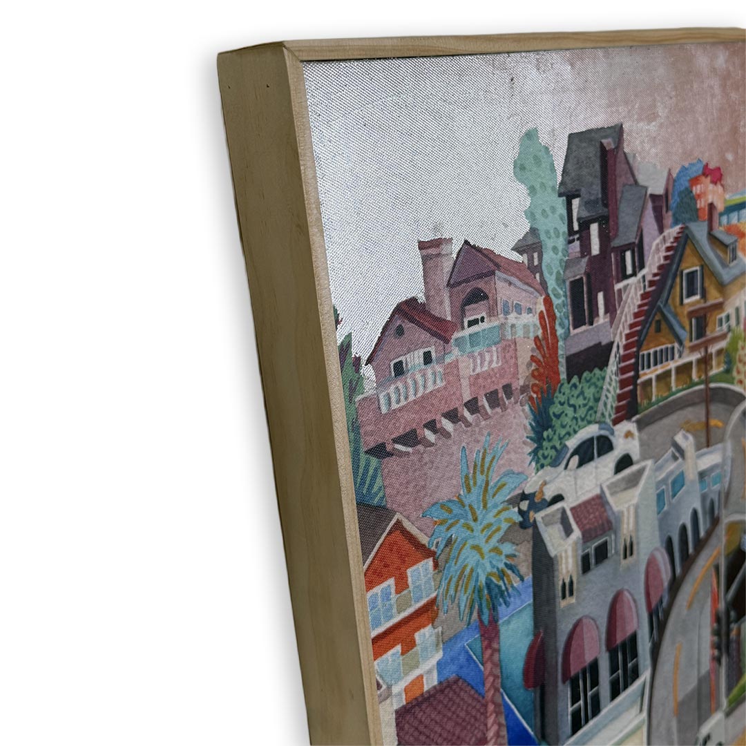 A close-up of a framed painting showing colorful houses and buildings with trees, photographed against a white background. Silver foil sky.