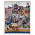 A framed colorful painting depicting a coastal hillside town with houses, palm trees, a curved road, beach umbrellas, and blue ocean water at the bottom. White background, silver foil sky.