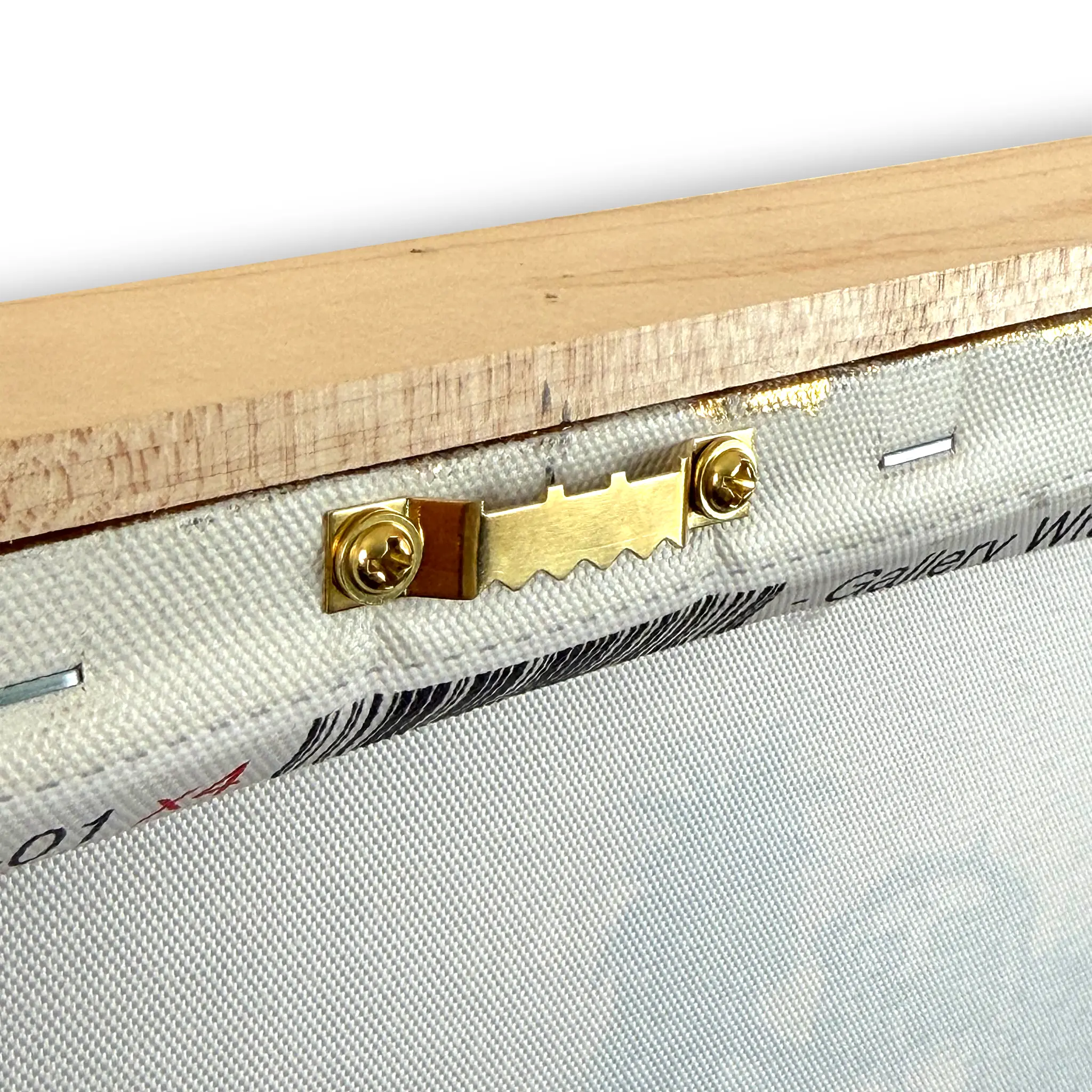 Close-up of a framed canvas or fabric panel showing the wooden stretcher bar, brass hanging hardware, and textured off-white fabric surface.